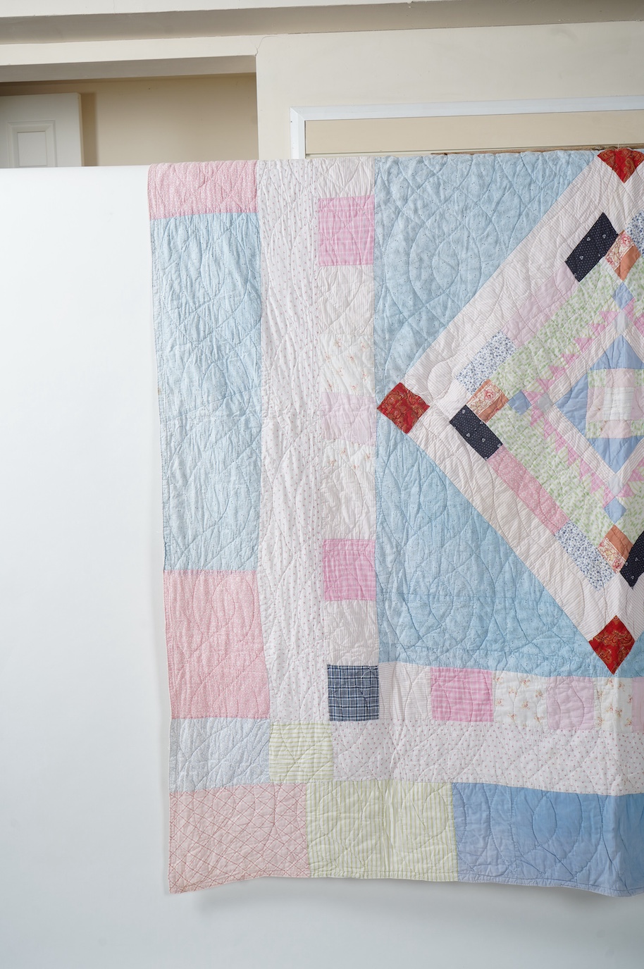 A 1900-1910 English, possibly north country hand quilted bedcover. Designed with a large central medallion, hand quilted using mostly pastel patterned and plain cottons and feature red and black cottons as highlights, ba